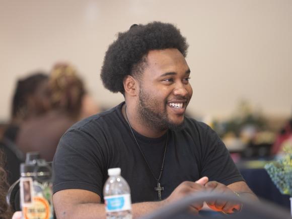 Student smiling in a classroom while listening to a professor speaking.