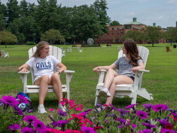 Two students sitting in Adirondack chairs surrounded by flowers on the campus green.