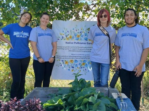 Four students stand in front of garden plants and a sign for Grandmothers' Garden