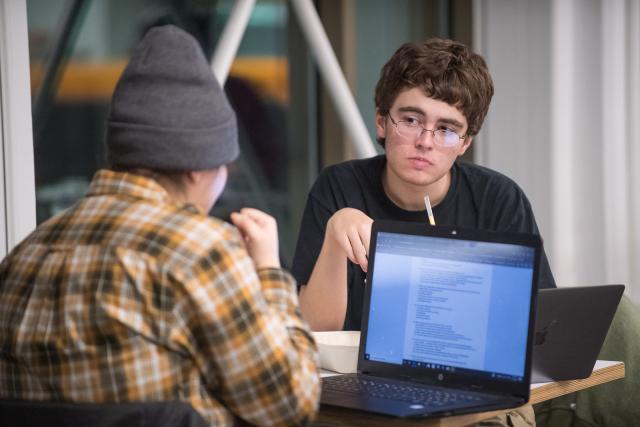 Two students talking to each other as they work on their laptops in the Ely Campus Center