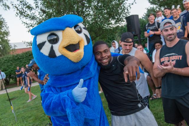 Nestor the Owl with his arm around a male student that the fall pep rally on the campus green