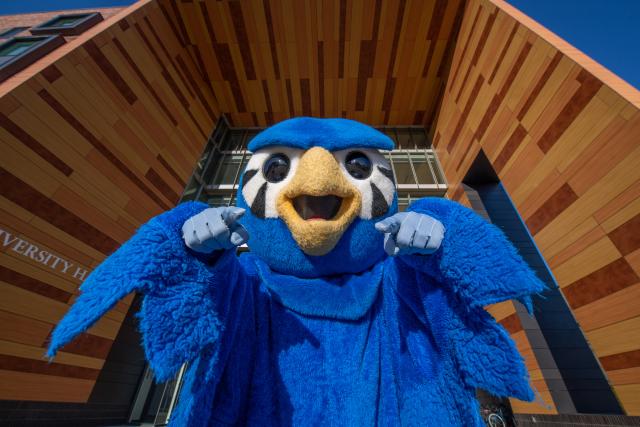 Nestor the Owl, pointing toward the camera, under the University Hall awning