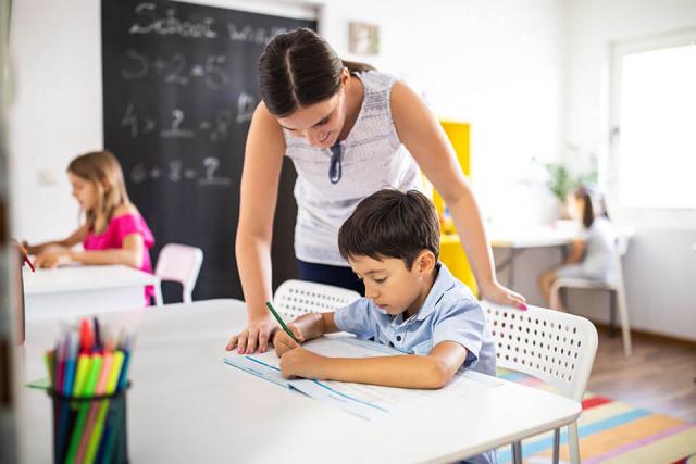 A teacher helps an elementary school–age student while they work on an assignment.