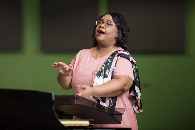 Felicia Barber conducts the WSU Chorale while standing at a podium.