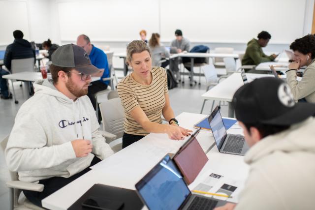 Economics instructor working one on one with a student wearing champion sweatshirt and baseball hat.