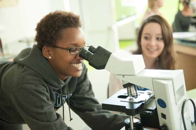 Student smiling looking through a microscope.