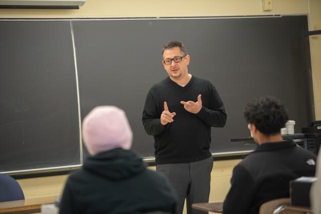 Faculty member delivering a lecture to students in a classroom setting.