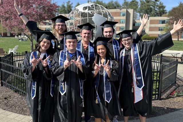 Group of students in caps and gowns smiling standing in front of the campus globe.