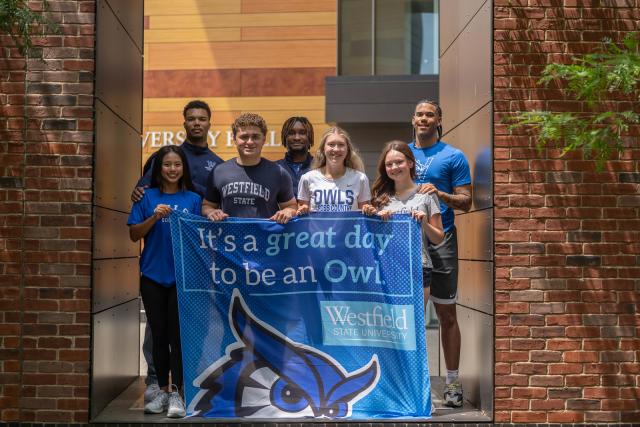 Smiling students holding a flag that reads 'It's a great day to be an Owl.'