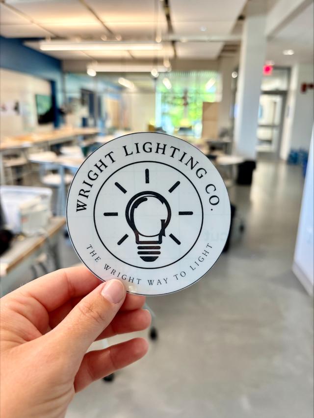 hand holding a round sticker labeled "wright lighting company" featuring a photo of a lightbulb outline