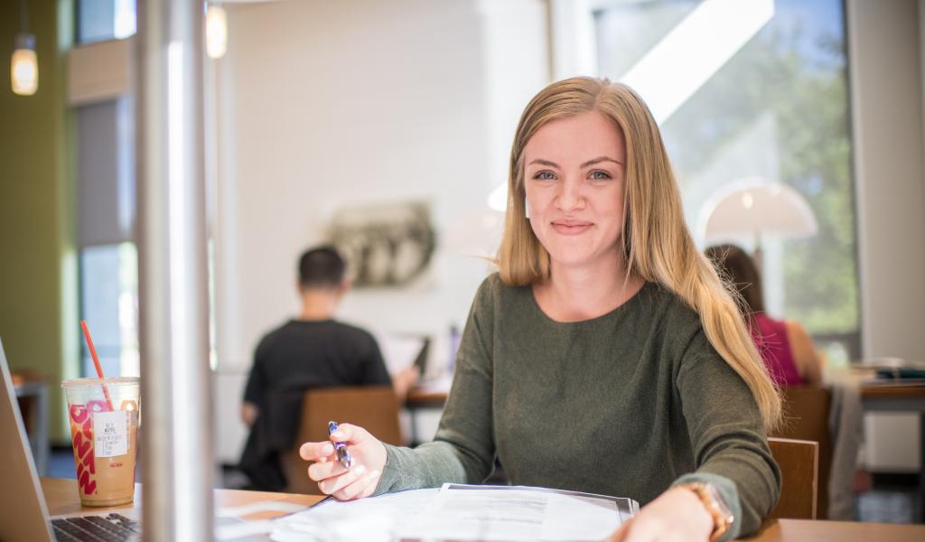 female student smiling at the camera as they work in the Ely Library