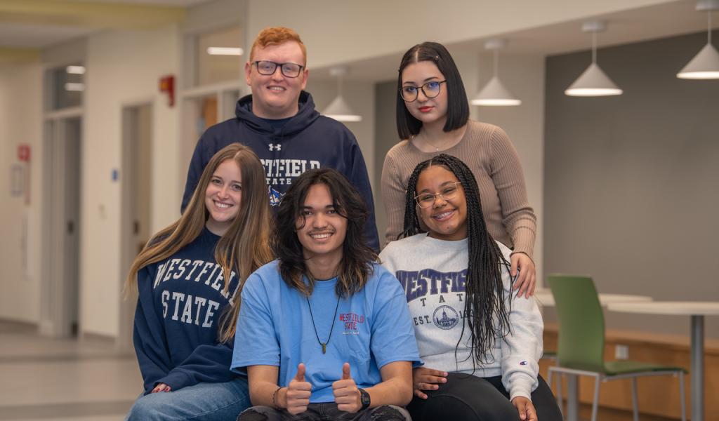 Five students in Parenzo Hall one with thumbs up. All students wearing WSU shirts smiling.