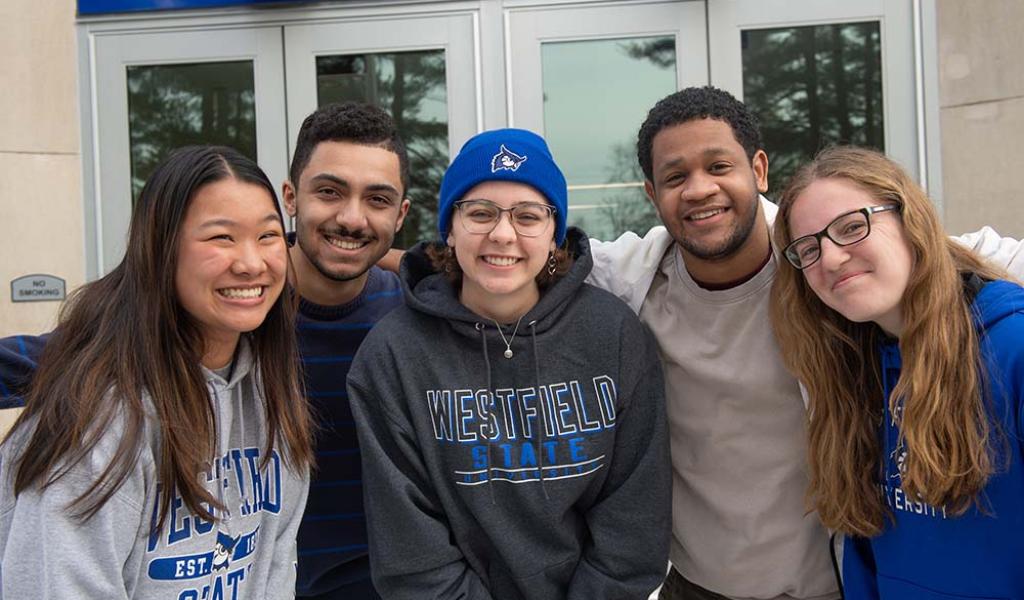 Five students huddle together and smile while posing for a photo.