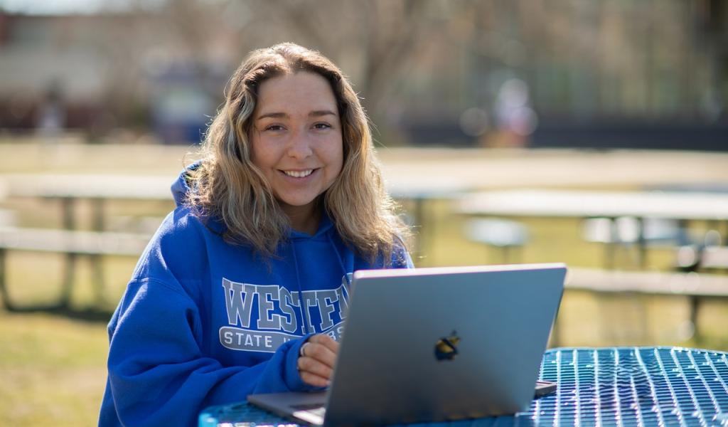Student studying outdoors focused on a laptop while working on a class assignment.