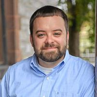 Joe member of the Western Mass Writing Project wearing light blue collared shirt smiling.