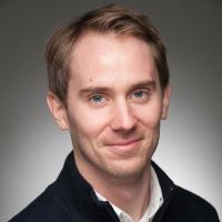 Colin Moge, class of 2016. He smiles in front of a plain, gray background, as part of his headshot. He is wearing a black sweater with a white shirt underneath. He has short, blond hair and blue eyes.