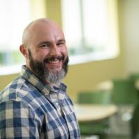 Dr. Alexander Moore smiling wearing a plaid shirt.