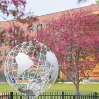 A photo of the campus globe. Two pink-flowered trees are planted on each side.