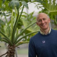 Tim Parshall, Professor of Environmental Science. He stands in front of trees in the Wilson Hall greenhouse.