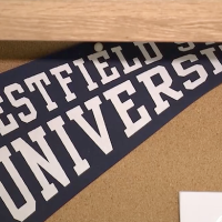 A close-up photo of a blue Westfield State University flag tacked to a cork board in a student dorm room.